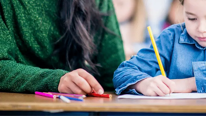 Adulto acompanhando uma criança que escreve no caderno