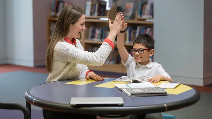 Professora e aluno batendo as mãos numa biblioteca